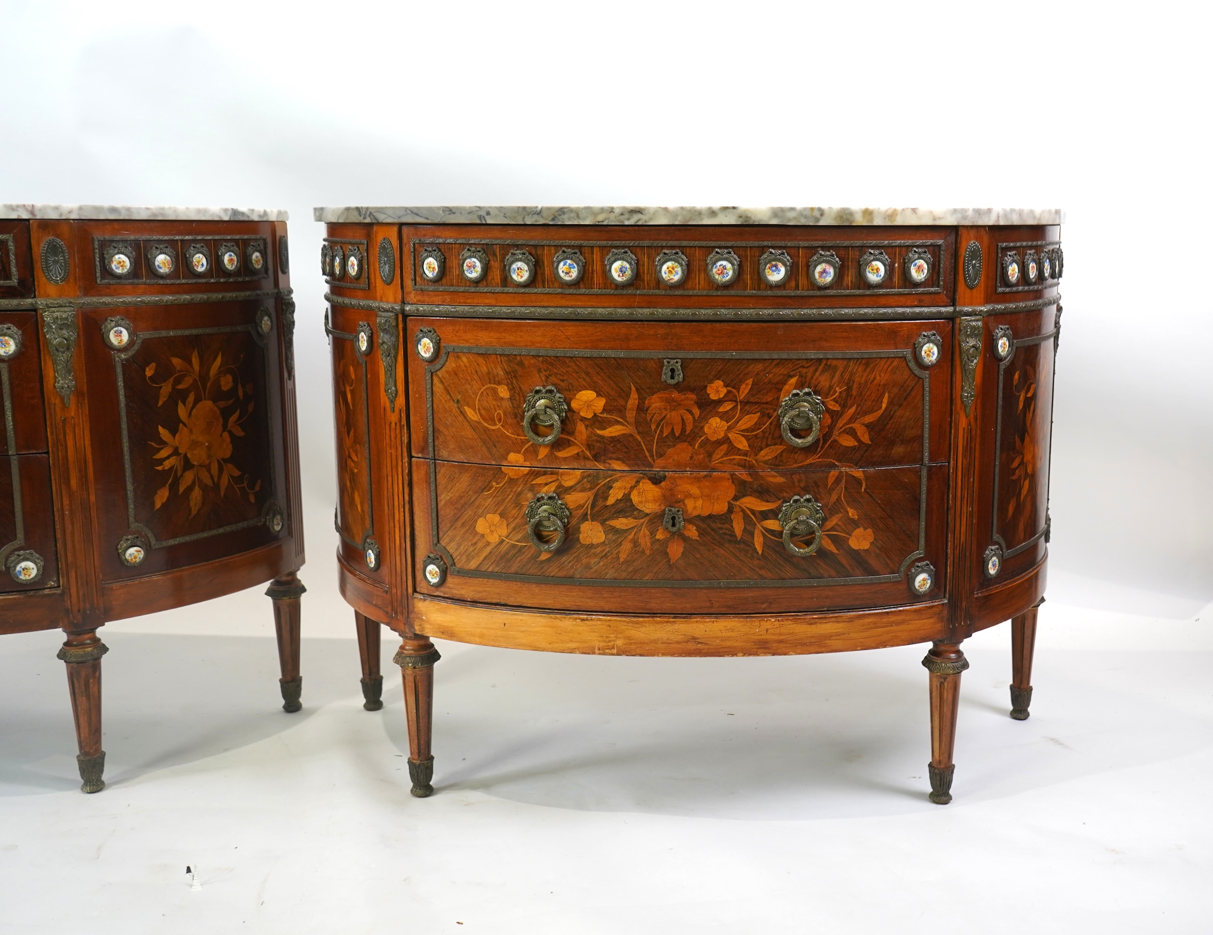 A pair of early 20th century French marquetry inlaid, gilt metal and porcelain mounted rosewood and beech demi-lune commodes